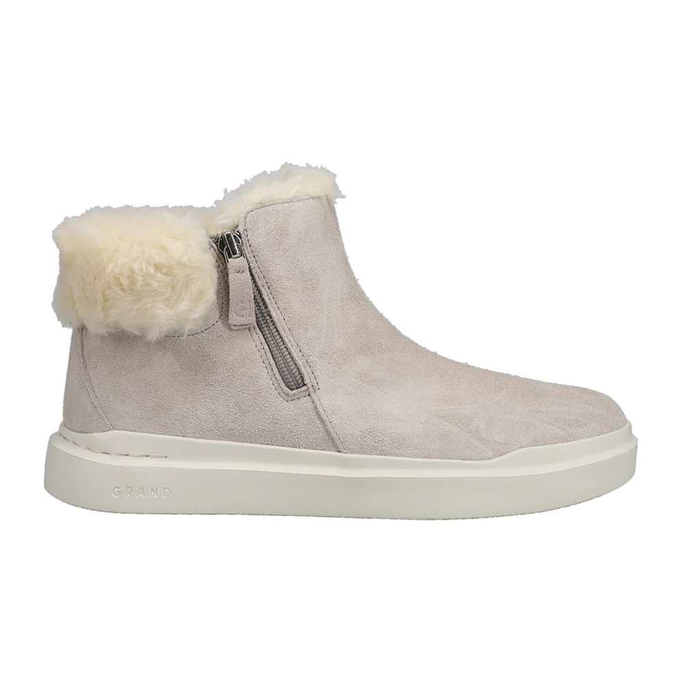 Cole Haan Zippered Snow Booties in light beige feature a suede exterior, shearling lining, and a side zipper for easy wear. The boot has a rubber sole for traction and is designed for warmth and comfort.