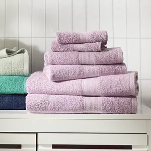 Stacked cotton towel set in various colors including purple, blue, and green, displayed on a white surface against a tiled wall.