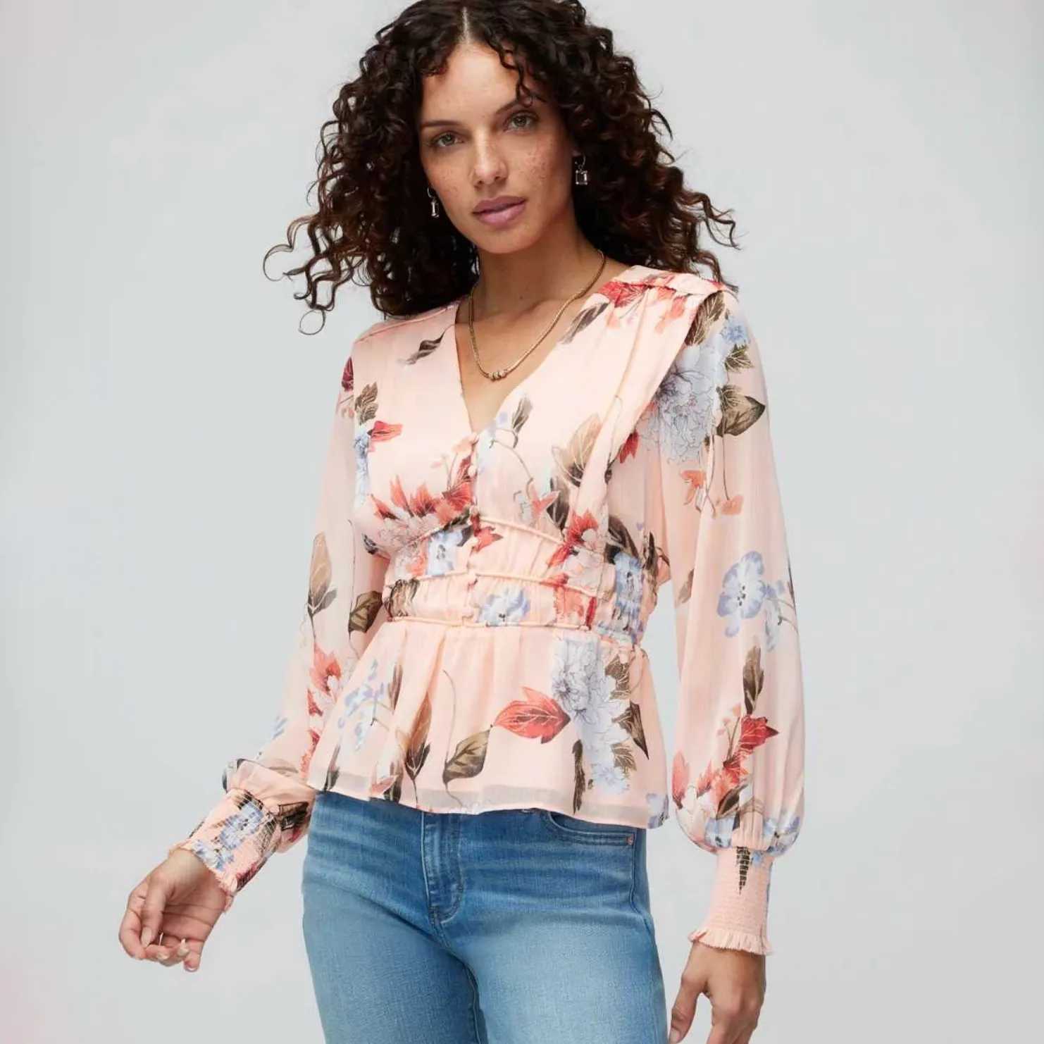 A woman is wearing a peach floral-print blouse with long sleeves and light blue jeans.
