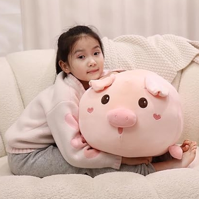A young girl is holding a large pink pig plush pillow with heart-shaped details and a smiling face.