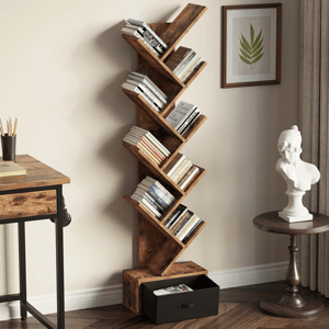 A wooden tree-style bookshelf with multiple angled shelves holds books and features a drawer at the bottom. Nearby is a small round table with a white bust sculpture and a framed leaf print on the wall.