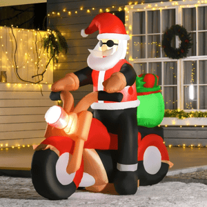 Inflatable Santa Claus wearing sunglasses is riding a motorcycle, with a green sack on the back, set in a festive outdoor scene with Christmas lights and a wreath.