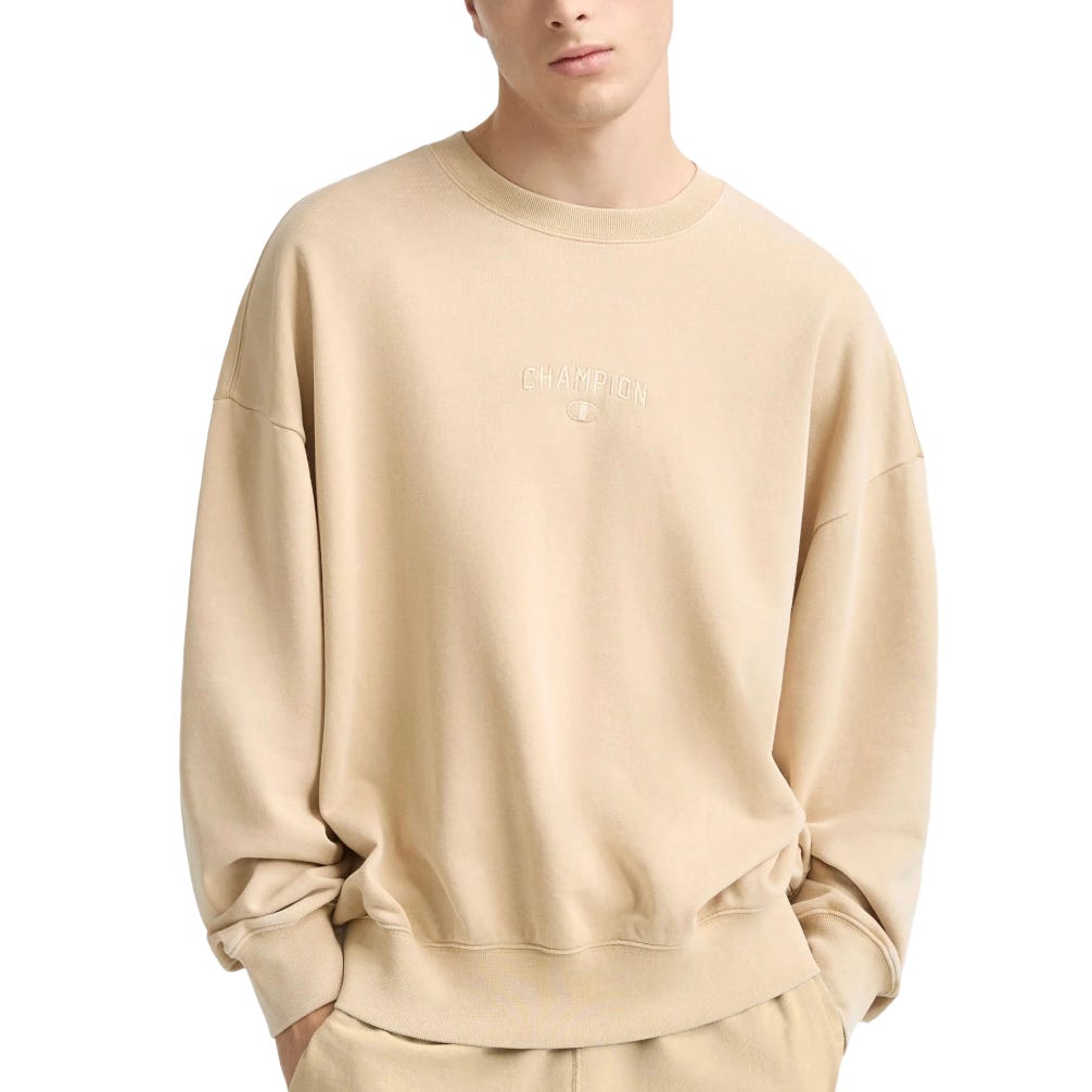 A beige Champion sweatshirt featuring an embroidered logo on the front, worn by a model paired with matching pants.
