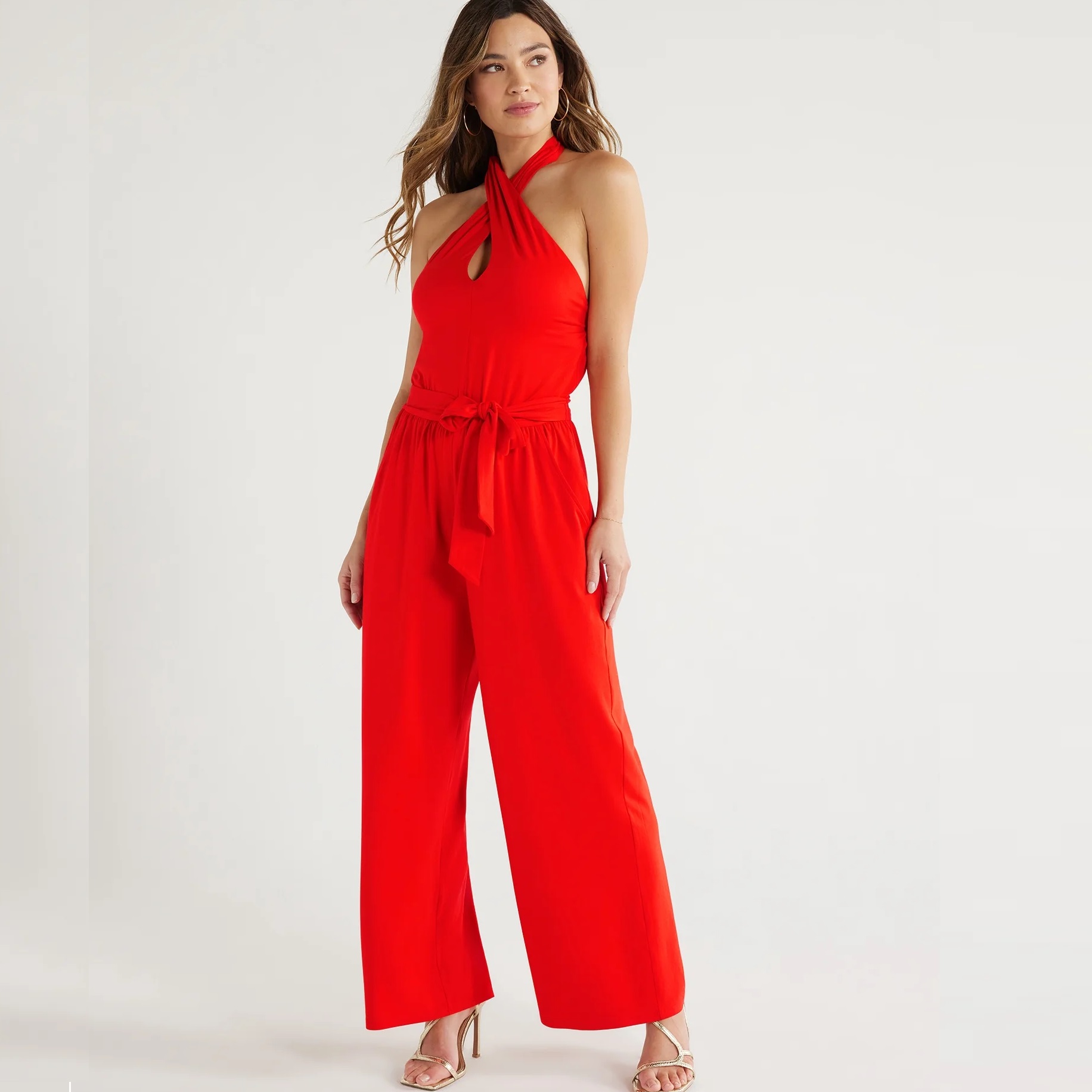 A woman models a sleeveless red jumpsuit with a halter neck and waist tie.