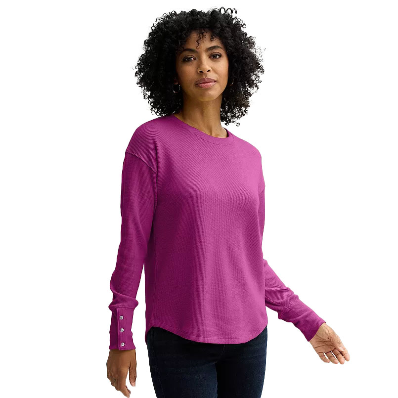 A woman wearing a purple long-sleeve waffle-knit top with button details on the cuffs and black jeans.