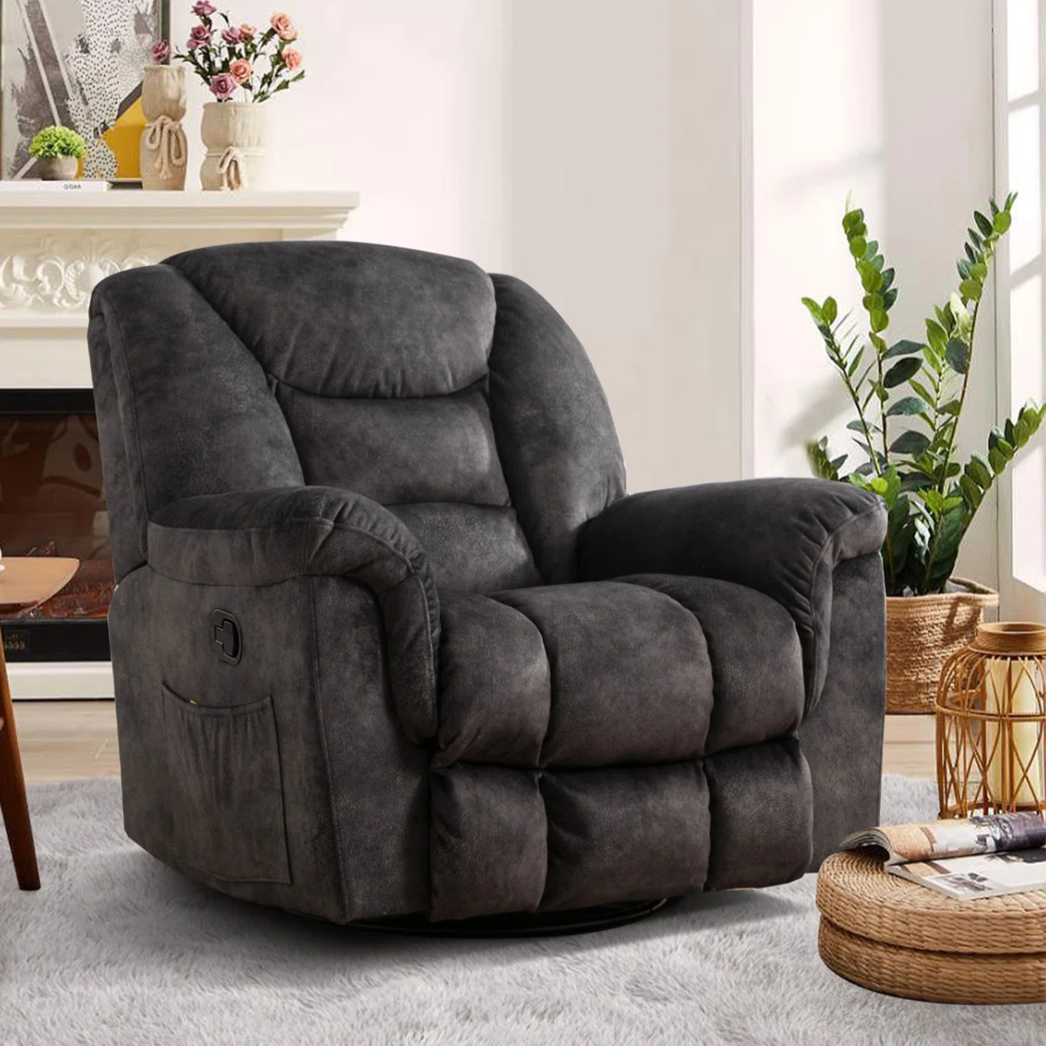 A plush dark gray recliner chair with padded armrests and a side pocket, set in a cozy living room with a light rug, a wooden table with a cup, and a woven basket with plants near a fireplace.