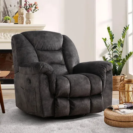 A plush dark gray recliner chair with padded armrests and a side pocket, set in a cozy living room with a light rug, a wooden table with a cup, and a woven basket with plants near a fireplace.