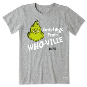 A gray women's t-shirt featuring the Grinch from Dr. Seuss with the text \“Greetings From WHO-VILLE\“ and \“Life is Good\“ printed in white. The Grinch's head is prominently displayed in green, adding contrast to the design.