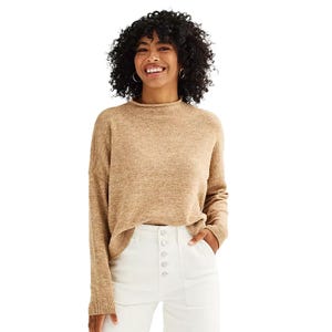 Woman wearing a beige turtleneck sweater and white high-waisted pants with button details.
