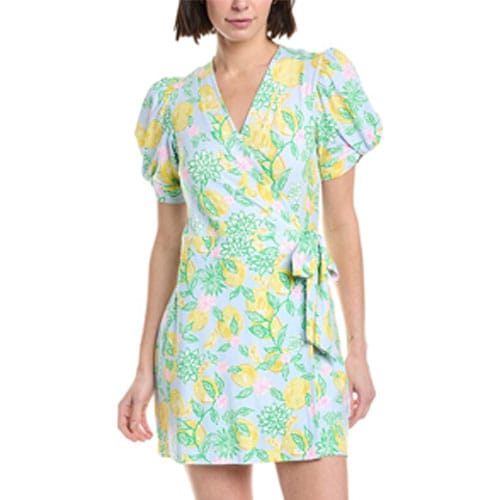 A woman wears a short, floral wrap dress with puffy short sleeves and a V-neck, featuring a pastel-colored pattern with green leaves and yellow flowers.