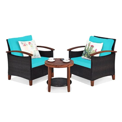Outdoor patio set with two wicker armchairs featuring turquoise cushions and decorative pillows, accompanied by a small round wooden side table.