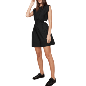 A woman is wearing a sleeveless black dress with a cinched waist, paired with black sneakers.