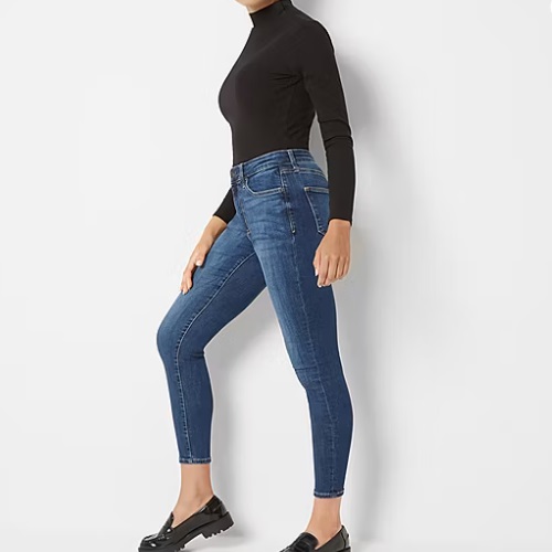 A person wearing a black turtleneck and blue skinny jeans stands sideways with one leg bent. They're also wearing black loafers with a chunky sole.