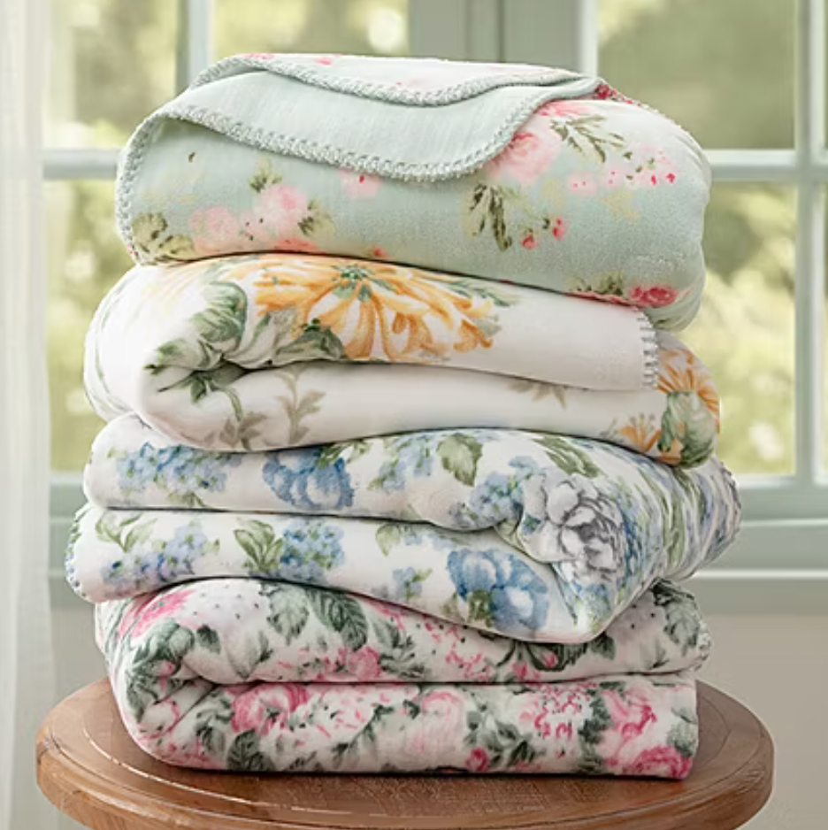 A stack of floral-patterned blankets in various colors, including blue, pink, and yellow, neatly folded on a wooden surface.