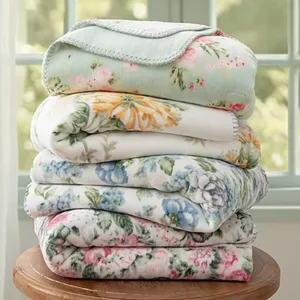 A stack of floral-patterned blankets in various colors, including blue, pink, and yellow, neatly folded on a wooden surface.