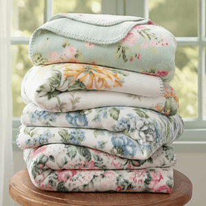 A stack of floral-patterned blankets in various colors, including blue, pink, and yellow, neatly folded on a wooden surface.