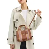 A person is wearing a light-colored trench coat and holding a brown handbag with purple and yellow woven handles and a shoulder strap.