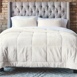 A neatly made bed features a tufted gray headboard, white pillows, and a plush cream comforter, set against a brick wall and atop a fluffy gray rug.