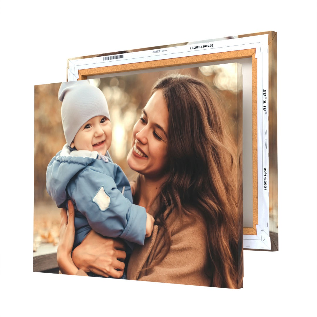 A canvas print featuring a smiling woman holding a baby dressed in a blue jacket and hat; the canvas is framed and measures 20x16 inches.