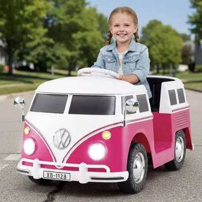 A child is driving a pink and white toy car resembling a vintage Volkswagen van, with a visible license plate reading \“XB-1128.\“