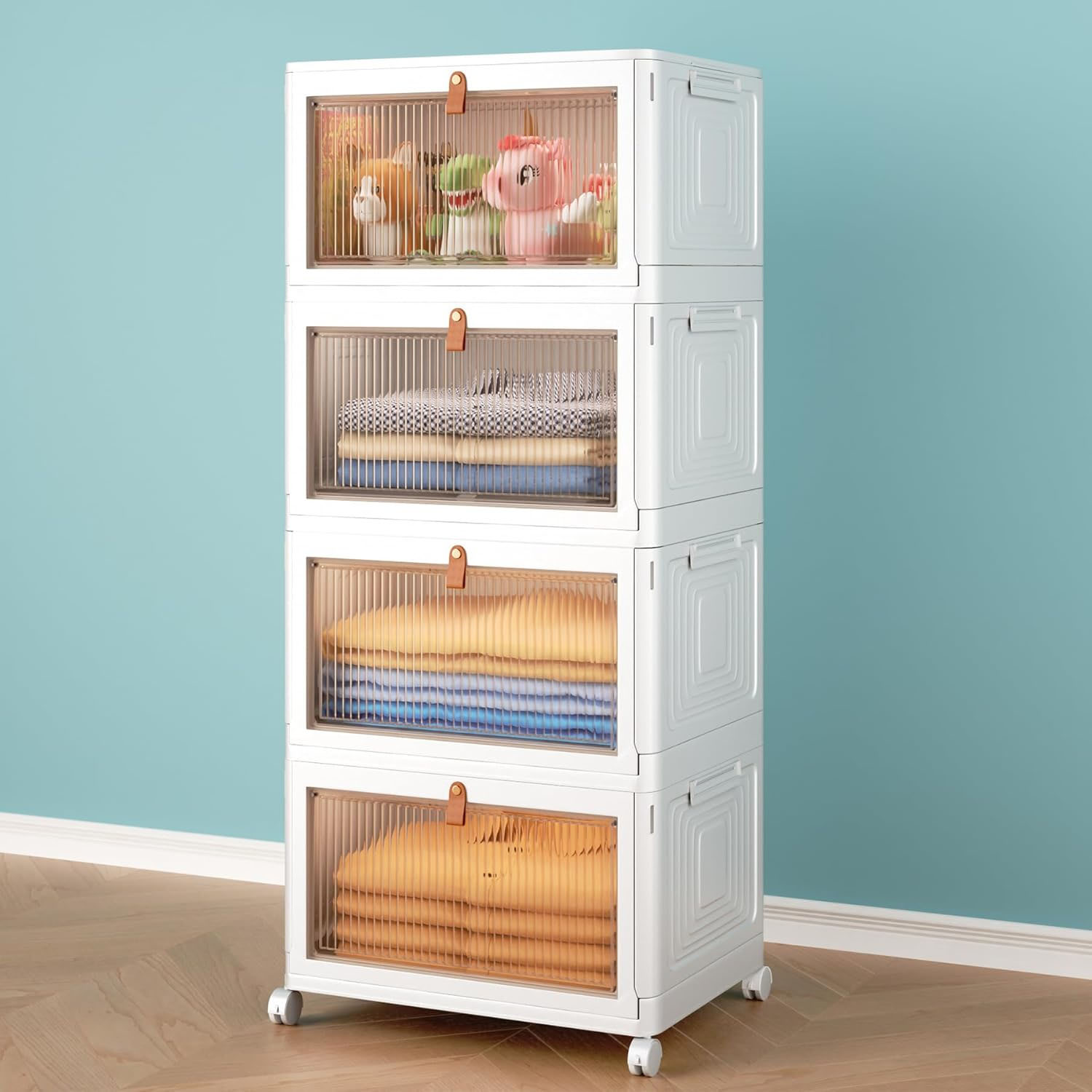 A white, four-tier storage unit with transparent doors on wheels, containing toys and folded clothes.