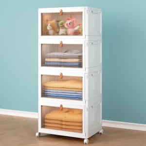 A white, four-tier storage unit with transparent doors on wheels, containing toys and folded clothes.
