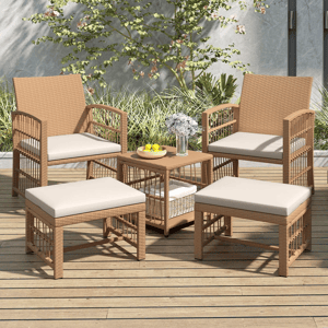 Outdoor patio set with two wicker chairs, two ottomans, and a small table. Cushions are beige, and the table holds a bowl of lemons and a vase with flowers. Surrounded by greenery on a wooden deck.