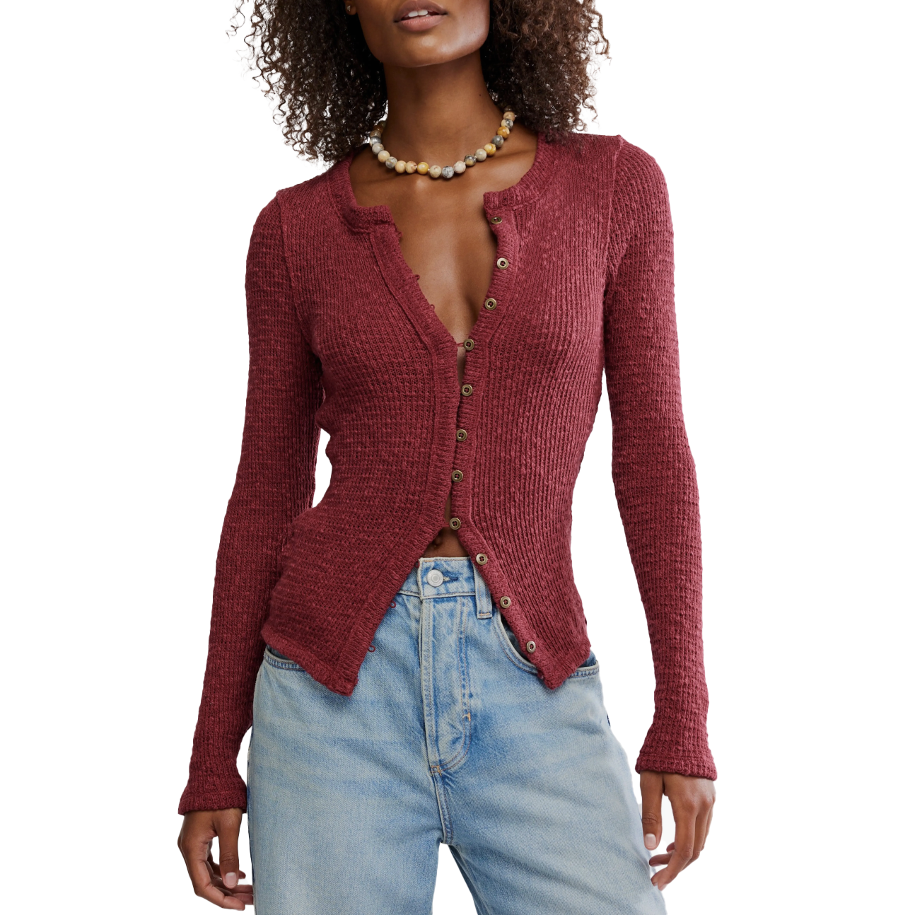 A woman is wearing a textured red cardigan with button details paired with light blue high-waisted jeans. She is accessorized with a beaded necklace.