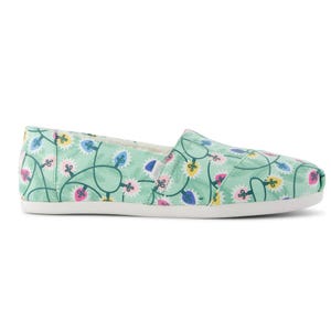 A casual slip-on shoe with a light green background and colorful, abstract floral pattern in pink, blue, and yellow.