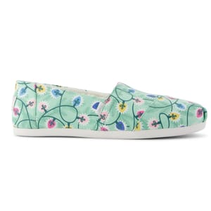 A casual slip-on shoe with a light green background and colorful, abstract floral pattern in pink, blue, and yellow.