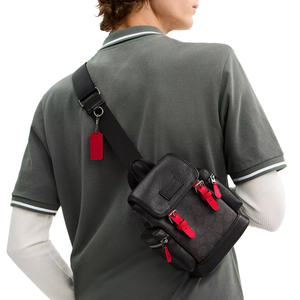 A person is wearing a black leather crossbody bag with red accents and zippers. The bag has multiple compartments and a visible brand tag hanging from the strap.