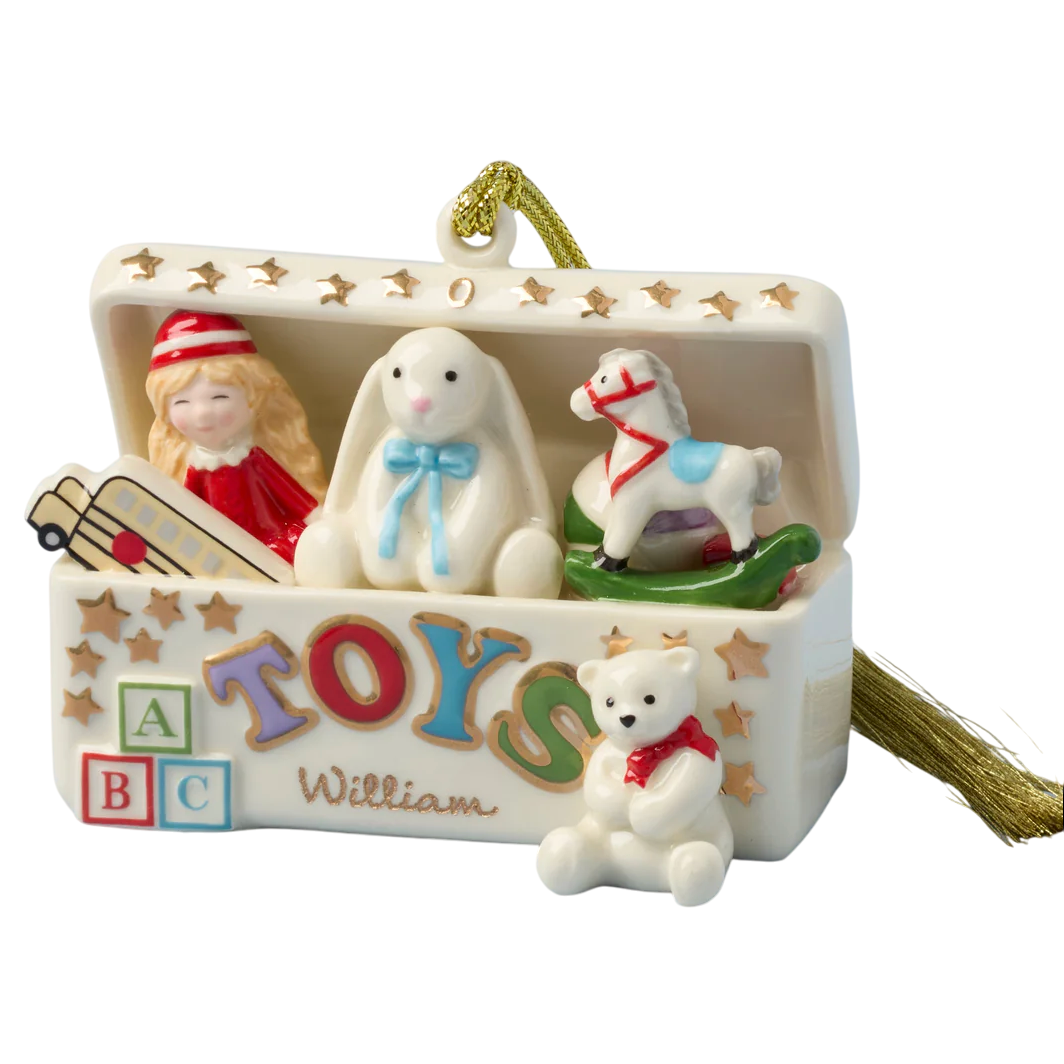 A ceramic ornament shaped like an open toy chest with a doll, bunny, rocking horse, and small toys. It has colorful letters spelling \“TOYS\“ and the name \“William\“ on the front, with a golden hanging string.