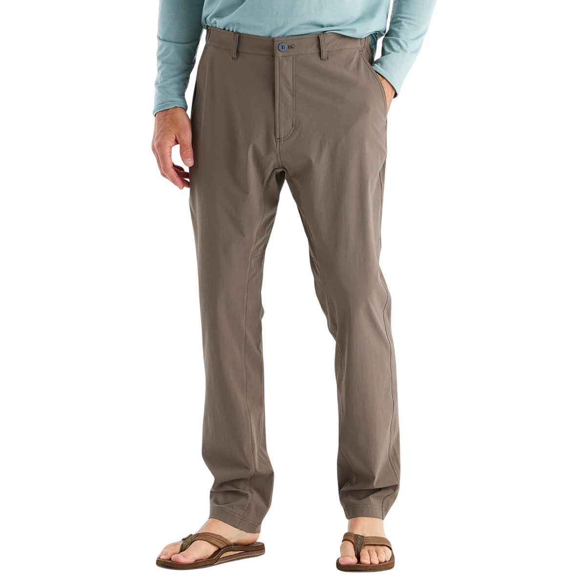 A person is wearing light brown khaki-style pants with a button closure and side pockets, paired with a light blue shirt and brown flip-flops.