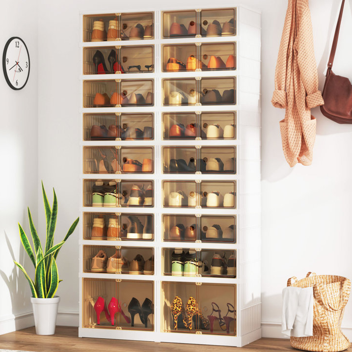Shoe storage cabinet with transparent doors, filled with various shoes, next to a potted plant, with a clock and a hanging bag on the wall.