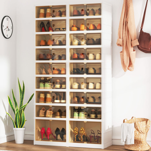 Shoe storage cabinet with transparent doors, filled with various shoes, next to a potted plant, with a clock and a hanging bag on the wall.