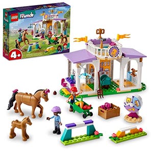 This LEGO Friends Horse Stable set includes a stable building, two horse figures, a mini-doll, a foal, accessories, and a tractor. The structure is adorned with purple and white detailing.
