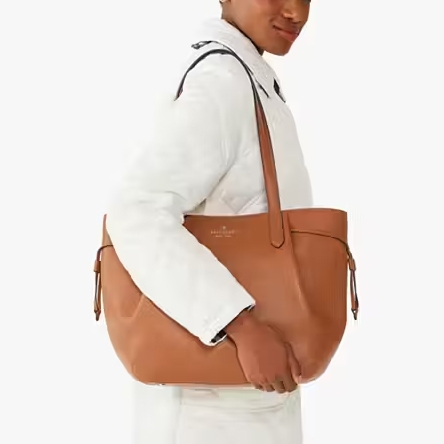 A person is carrying a large tan leather shoulder bag with a top handle and a visible logo.