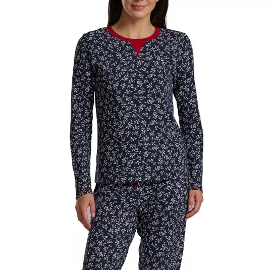 A woman is wearing a long-sleeve pajama set with a navy blue background and a small, white floral pattern. The pajamas feature a contrasting red neckline.