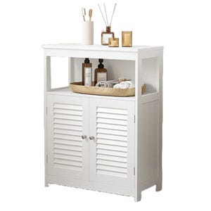 A white cabinet with shutter-style doors features an open upper shelf for storage or display. Items on the top include a wood tray with bottles, a rolled towel, and decorative elements like candles and reed diffusers.