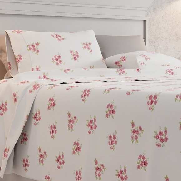 A bed is dressed with white sheets adorned with a floral pattern featuring small red and pink flowers, accompanied by matching pillowcases.