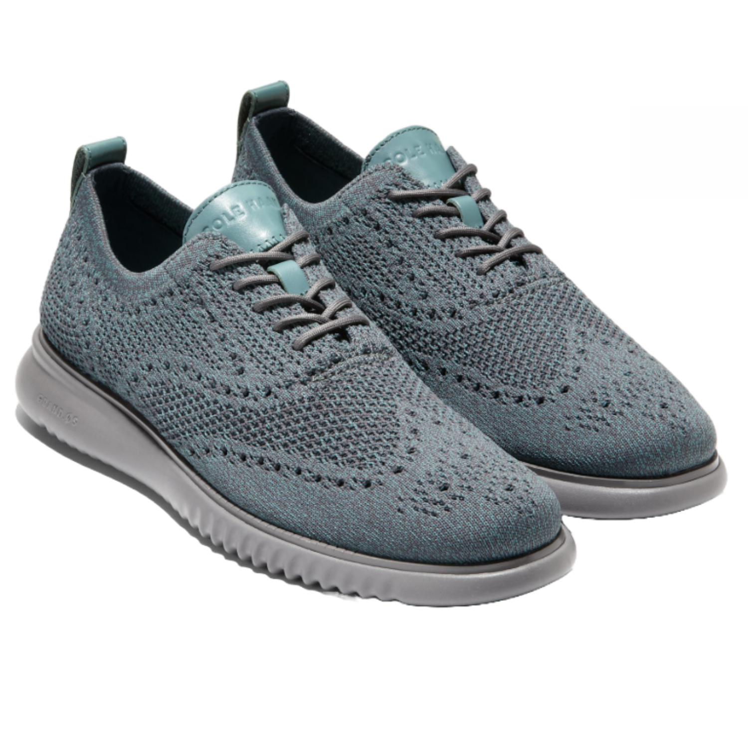 Cole Haan Men's ZeroGrand Oxfords are lightweight knit shoes featuring a wingtip design in a greyish-blue tone with a flexible grey sole. They offer a modern blend of style and comfort.
