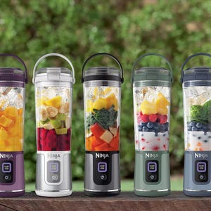 Four portable blender cups filled with fruits and ice, each with a Ninja logo and a control button.
