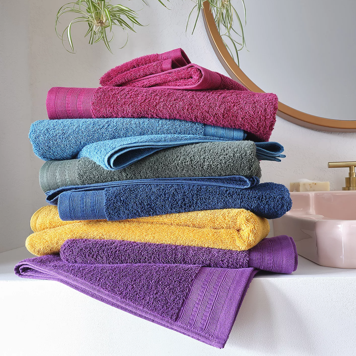 A stack of colorful bath towels in shades of pink, blue, gray, yellow, and purple.