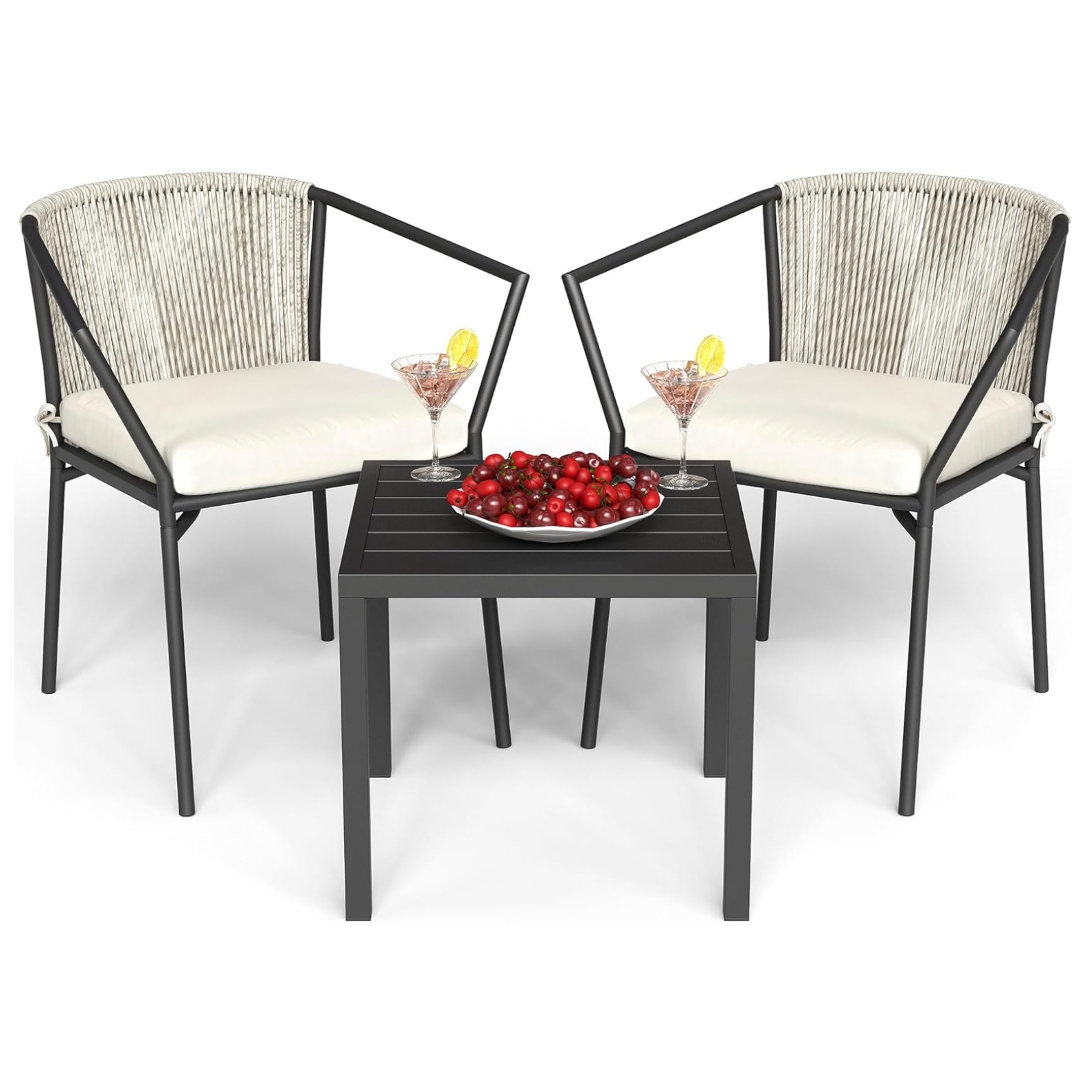 Two modern patio chairs with armrests and white cushions sit beside a small black table. The table holds a bowl of cherries and two cocktail glasses with lemon slices.