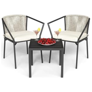 Two modern patio chairs with armrests and white cushions sit beside a small black table. The table holds a bowl of cherries and two cocktail glasses with lemon slices.