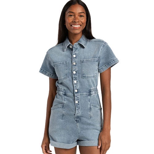 A woman is wearing a denim short-sleeve romper with two chest pockets and front button closure.