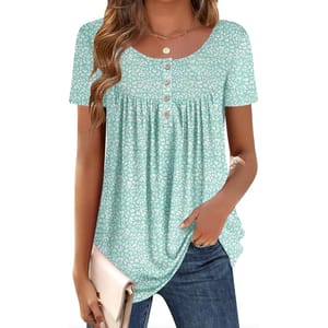 A woman is wearing a light teal short-sleeve top with a white floral pattern and button details on the front, paired with blue jeans and holding a light beige clutch.