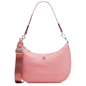 A pink lululemon shoulder bag with a rounded design, featuring an adjustable fabric strap and a silver logo on the front.