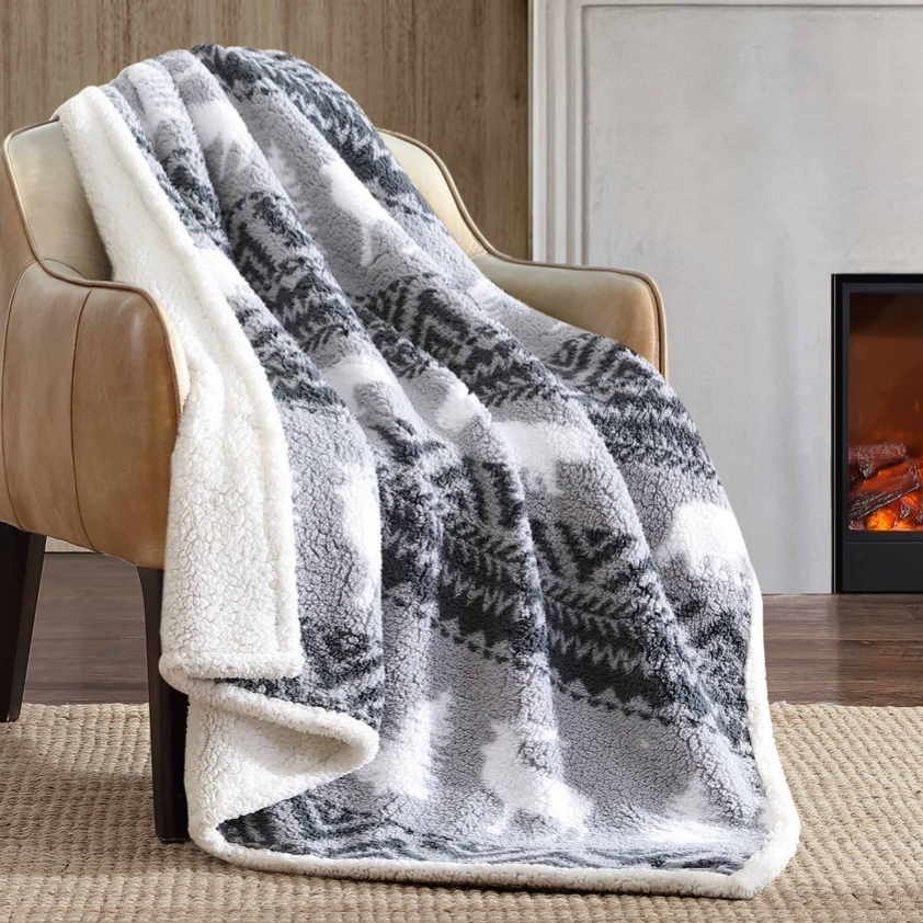 A cozy gray and white fleece blanket with a pattern is draped over a tan leather chair. The setting includes a fireplace and a snowy scene outside the window.