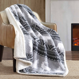 A cozy gray and white fleece blanket with a pattern is draped over a tan leather chair. The setting includes a fireplace and a snowy scene outside the window.